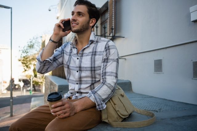Young man talking on mobile phone while sitting on retaining wall