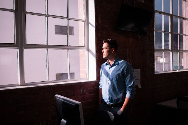 Thoughtful caucasian businessman standing alone in office looking out of window - Download Free Stock Photos Pikwizard.com