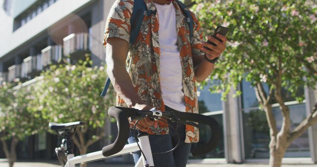 Midsection of african american man in city, wheeling bike and using smartphone in the street. digital nomad on the go, out and about in the city.