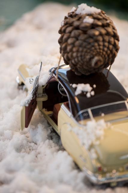 Toy car carrying pine cone on fake snow during christmas time