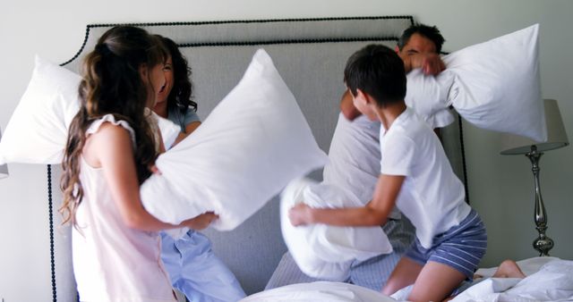 A family engages in a playful pillow fight on a bed, with copy space - Download Free Stock Photos Pikwizard.com
