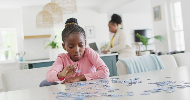 Happy african american granddaughter doing jigsaw puzzle, with grandmother in background, copy space. Relaxation, learning, family and domestic life.