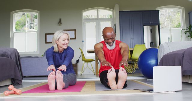 Mixed race senior couple performing stretching exercise looking at laptop at home. retirement and active senior lifestyle concept
