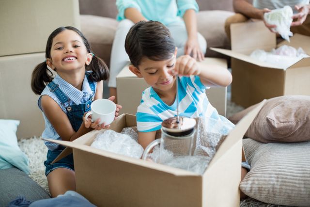 Portrait of kids unpacking carton boxes in living room at new home