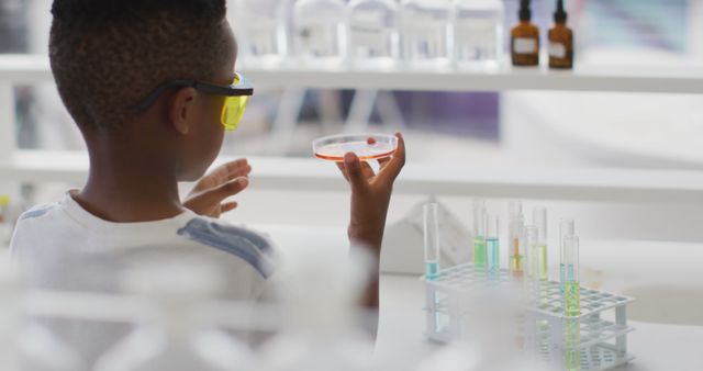 Image of happy african american boy wearing glasses and holding reagent during chemistry lesson. primary school education and learning concept.