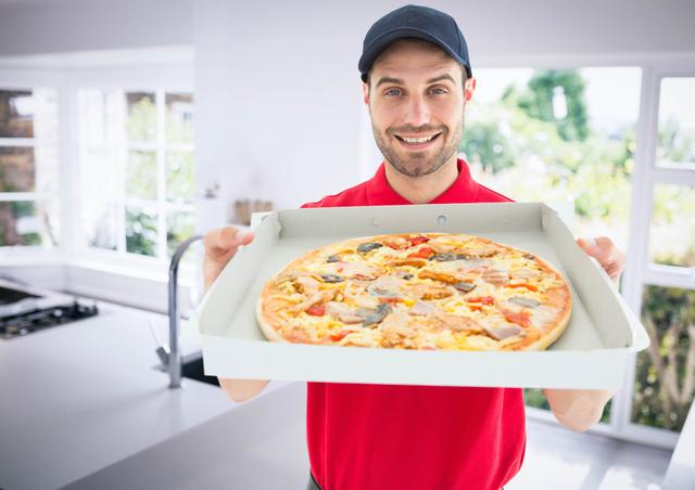 Happy deliveryman showing the pizza in the kitchen - Download Free Stock Photos Pikwizard.com