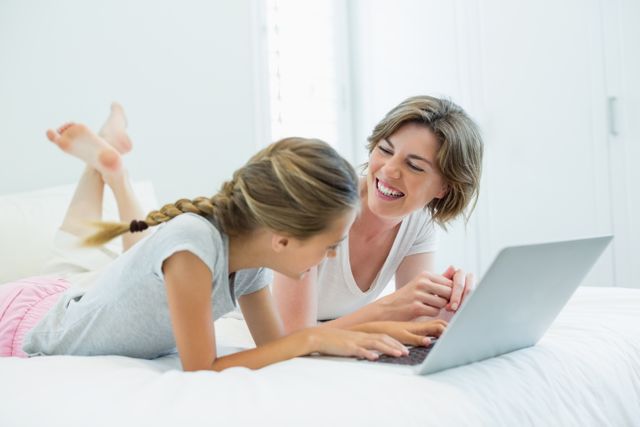 Mother and daughter interacting with each other while using laptop on bed - Download Free Stock Photos Pikwizard.com