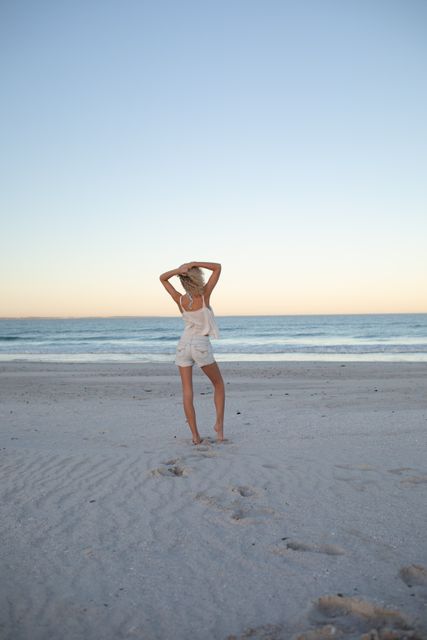 Woman standing with hands behind head on the beach- Download Free Stock Photos Pikwizard.com