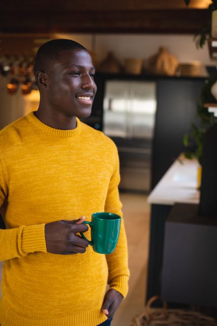 Thoughtful african american young man holding coffee cup looking away while standing at home. Copy space, unaltered, contemplation, lifestyle, drink and technology concept.