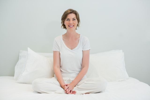 Smiling woman sitting cross legged on bed in bedroom at home - Download Free Stock Photos Pikwizard.com