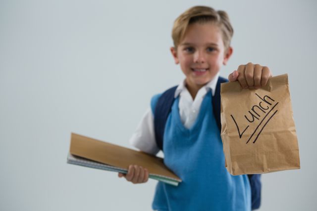 Smiling schoolboy holding book and lunch paper bag - Download Free Stock Photos Pikwizard.com