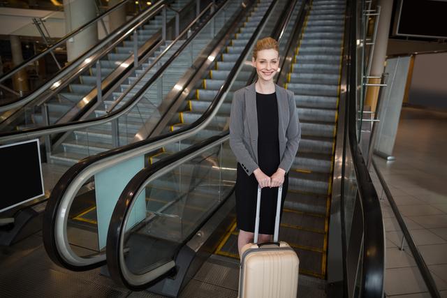 Businesswoman standing near escalator with luggage - Download Free Stock Photos Pikwizard.com