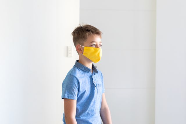 Little caucasian boy walking around the house wearing a yellow facemask - Download Free Stock Photos Pikwizard.com