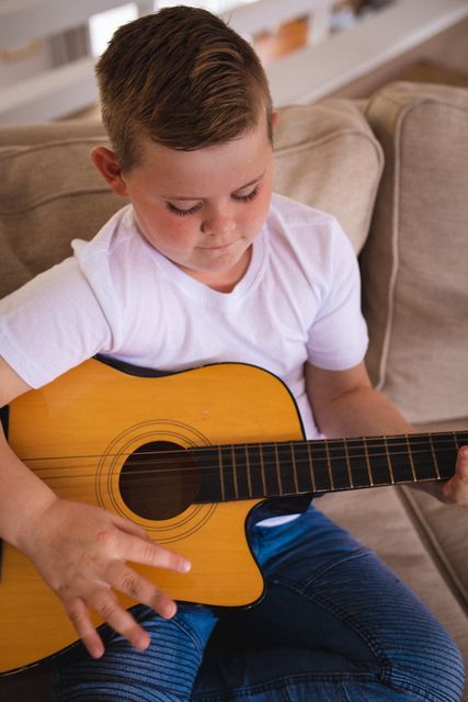 Caucasian boy playing guitar sitting on the couch at home - Download Free Stock Photos Pikwizard.com
