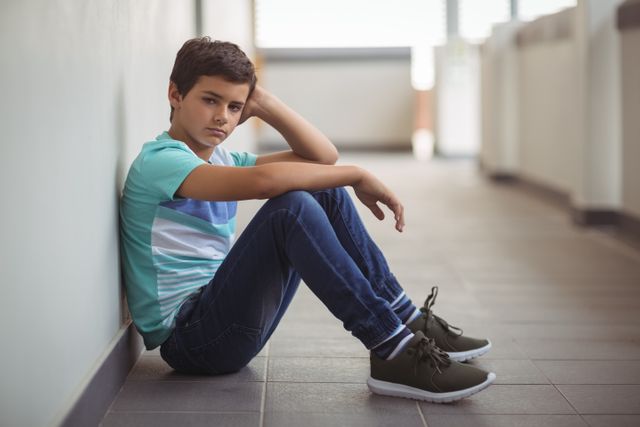 Portrait of sad schoolboy sitting in corridor - Download Free Stock Photos Pikwizard.com
