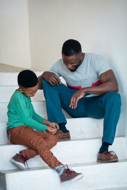 African american son tying shoes to his father on stairs - Download Free Stock Photos Pikwizard.com