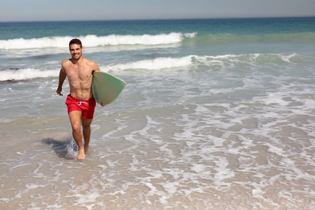 Shirtless man with surfboard walking on beach in the sunshine - Download Free Stock Photos Pikwizard.com