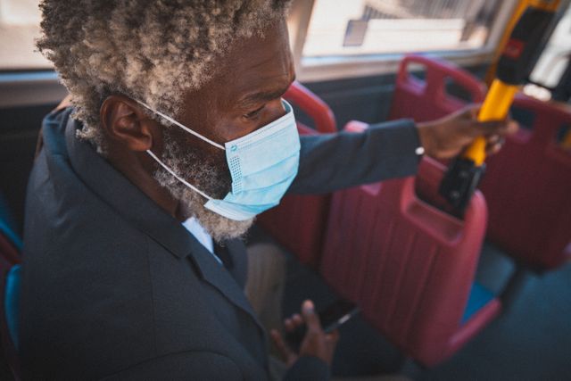 African american senior man wearing face mask sitting in public bus holding smartphone - Download Free Stock Photos Pikwizard.com
