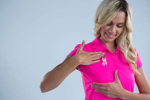 Smiling woman with pink ribbon touching on breast - Download Free Stock Photos Pikwizard.com