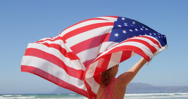 A Caucasian woman holds an American flag high on a sunny beach, with copy space - Download Free Stock Photos Pikwizard.com