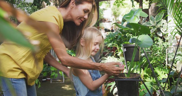 Happy caucasian mother and daughter touching plants in sunny garden. Family, nature, gardening and hobbies.