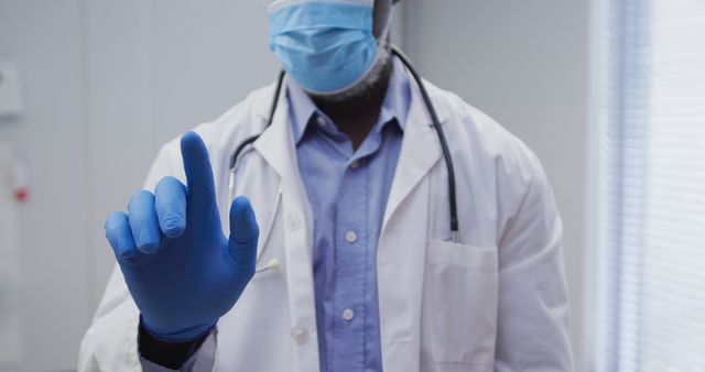 Midsection of african american male doctor wearing face mask and surgical gloves. medicine, health and healthcare services during coronavirus covid 19 pandemic.