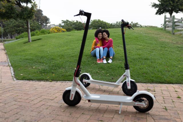 Twins embracing each other in a park with electric scooters in front - Download Free Stock Photos Pikwizard.com