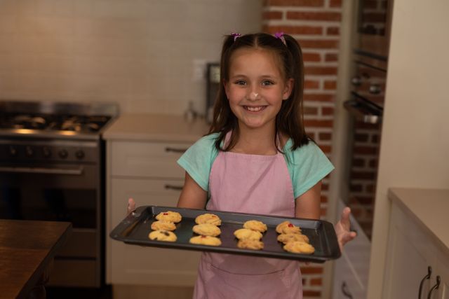 A caucasian girl wearing an apron in the kitchen holding a tray of cookies up with a smile on her fa - Download Free Stock Photos Pikwizard.com