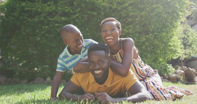 Portrait of happy african american parents and son embracing and smiling in garden. Lifestyle, domestic life, family, and togetherness.