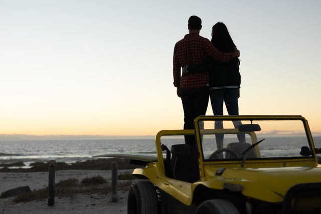 Happy couple standing in beach buggy by sea at sunset, admiring the view. beach stop off on romantic summer holiday road trip.