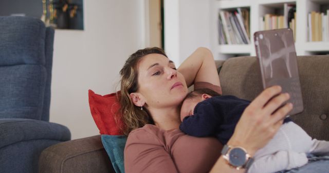 Image of caucasian mother with tablet lying on sofa with newborn sleeping baby - Download Free Stock Photos Pikwizard.com