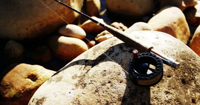 Close-up of a fly-fishing rod, reel, fly line, and pink fly on a rock  background. Stock Photo