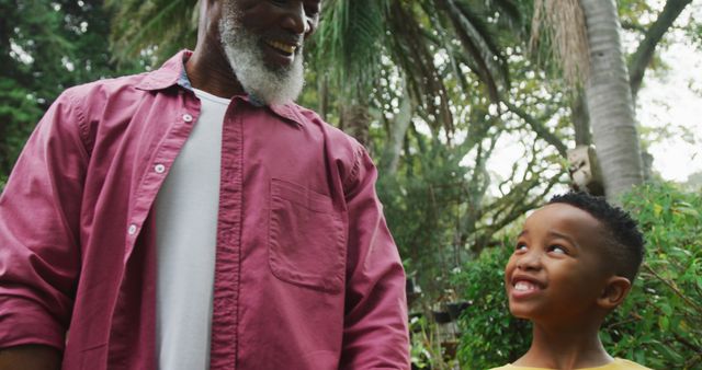 Happy senior african american man with his grandson walking together in garden. Spending time outdoors, working in garden nursery.