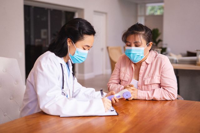 Asian female doctor and patient wearing face masks during medical visit - Download Free Stock Photos Pikwizard.com
