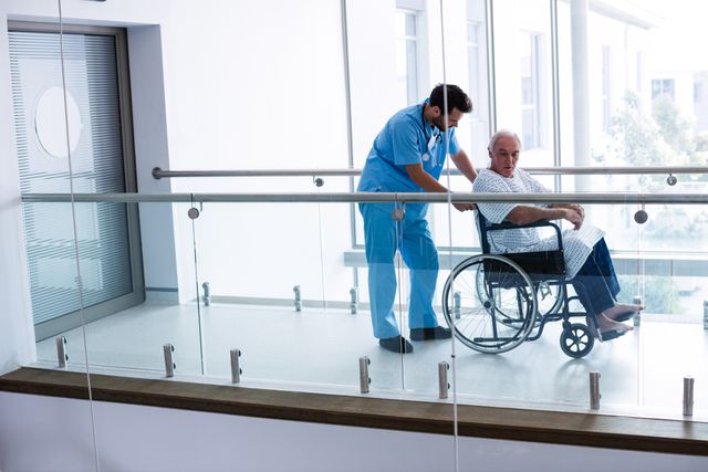 Male doctor pushing senior patient on wheelchair in passageway at hospital