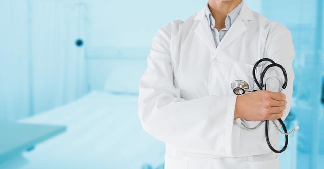 Mid section of doctor wearing laboratory coat and holding stethoscope in hospital