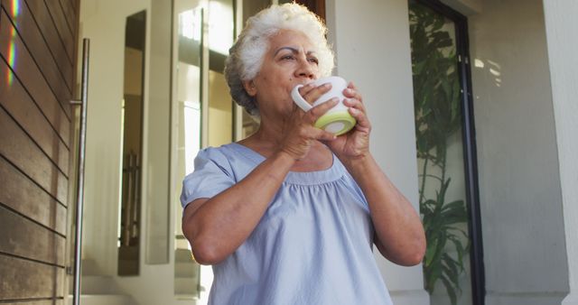 African american senior woman drinking coffee while standing at the front door at home. retirement senior lifestyle living in quarantine lockdown concept