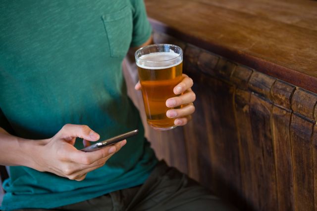Midsection of man using phone while having beer - Download Free Stock Photos Pikwizard.com