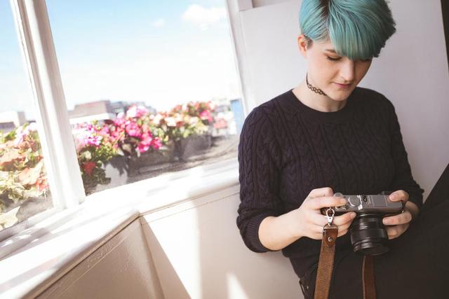 Une fille avec une coiffure courte et des cheveux bleus portant un pull se tient devant la fenêtre et regarde la caméra - Des images rétro plus créatives seront adaptées au public moderne en 2019 - Image