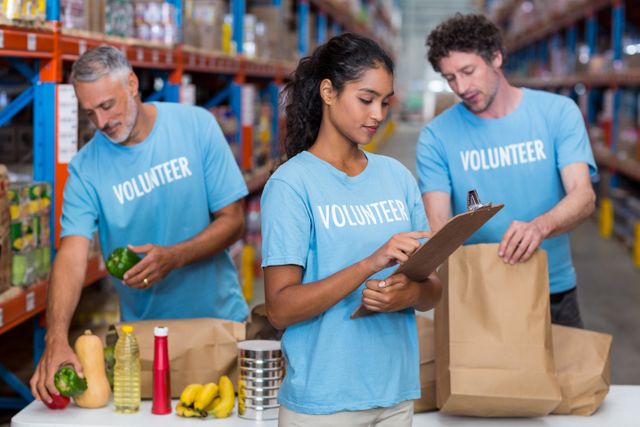 Three volunteers packing eatables in cardboard box in a warehouse - Download Free Stock Photos Pikwizard.com