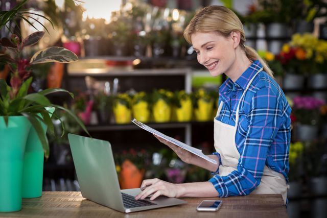 Female florist using laptop while holding clipboard - Download Free Stock Photos Pikwizard.com