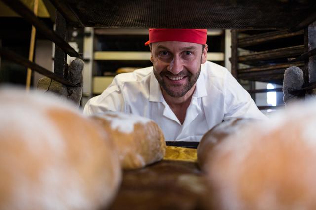 Portrait of smiling baker keeping tray of baked buns in shelf