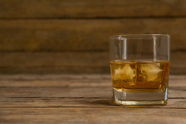 Glass of whisky with ice cube on wooden table - Download Free Stock Photos Pikwizard.com