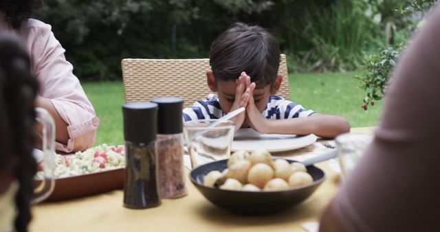Biracial boy praying at table with meal in garden - Download Free Stock Photos Pikwizard.com