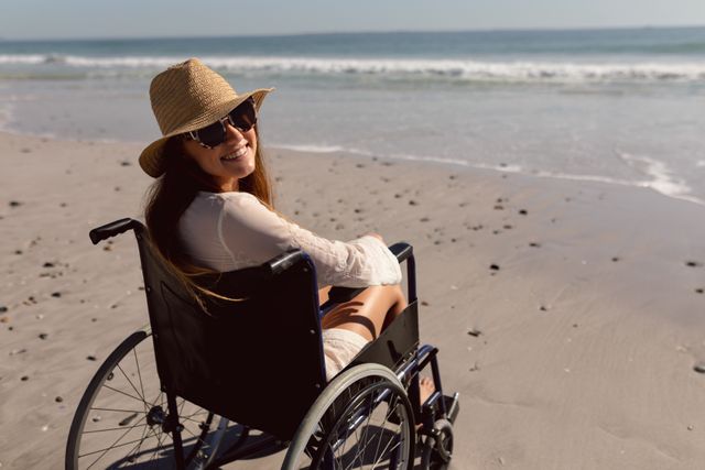 Disabled woman in hat and sunglasses sitting on wheelchair at beach in the sunshine - Download Free Stock Photos Pikwizard.com