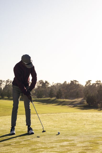 Full length of african american young man hitting ball with golf club on field against clear sky. Copy space, golf course, golf, unaltered, nature, sport and weekend activities concept.