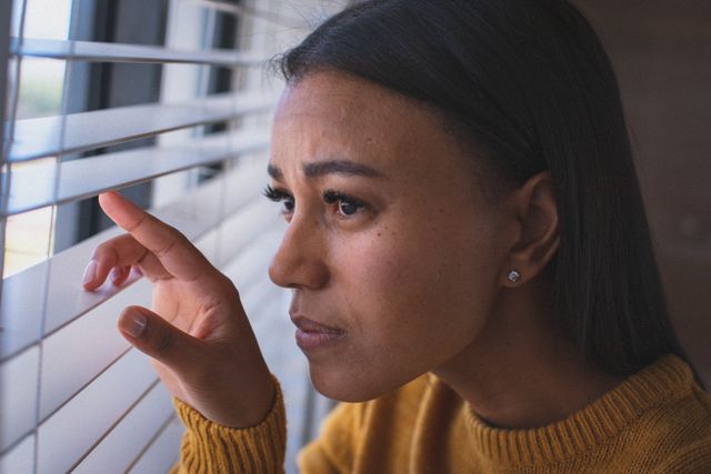 Mixed race woman peering through venetian blinds and looking out of window. staying at home in isolation during quarantine lockdown.