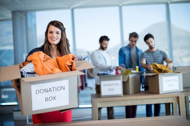 Smiling woman holding a donation box in office - Download Free Stock Photos Pikwizard.com