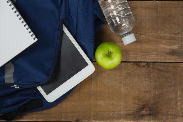 Schoolbag, apple, water bottle, book and digital table on wooden table - Download Free Stock Photos Pikwizard.com
