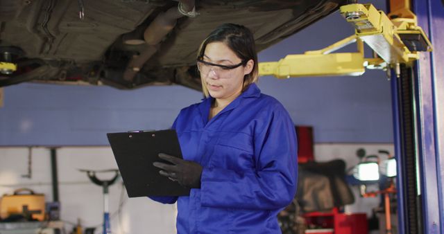 Portrait of female mechanic taking notes on clipboard and smiling at a car service station. automobile repair service
